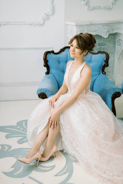Beautiful bride in a delicate wedding dress sits on a chair and waits for the groom. The concept of true untold love. Sincere feeling of a girl on a wedding day. - Photo, Image