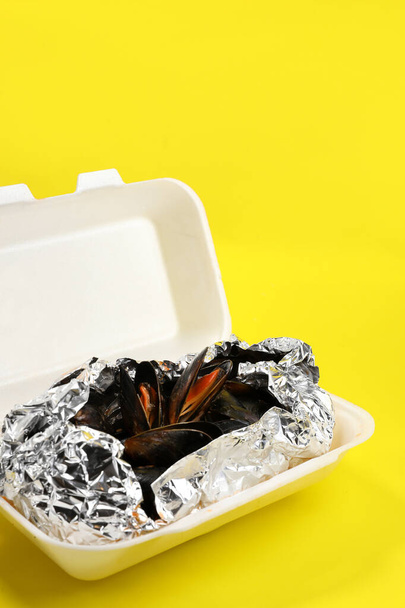 Livraison de nourriture en emballage plastique à votre domicile. Moules en sauce en papier d'aluminium et récipient en plastique sur fond jaune - Photo, image