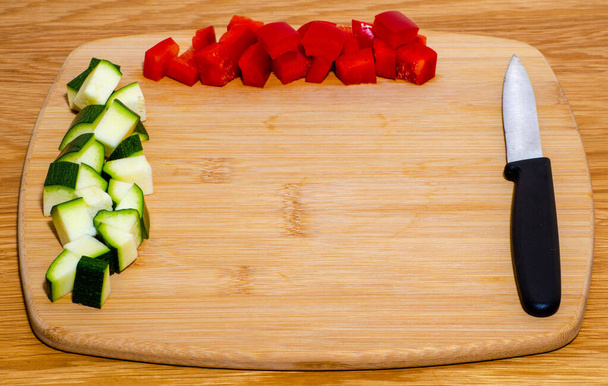 Diced pepper and courgette arranged on wood chopping board with knife and wooden background with selective focus and copy space - Photo, Image