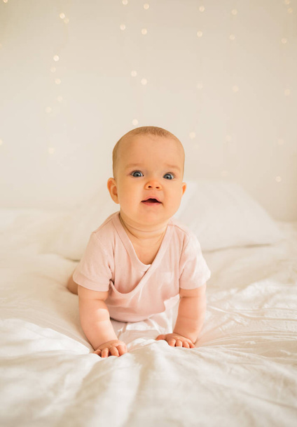 klein meisje in roze bodysuit kruipt op het bed - Foto, afbeelding