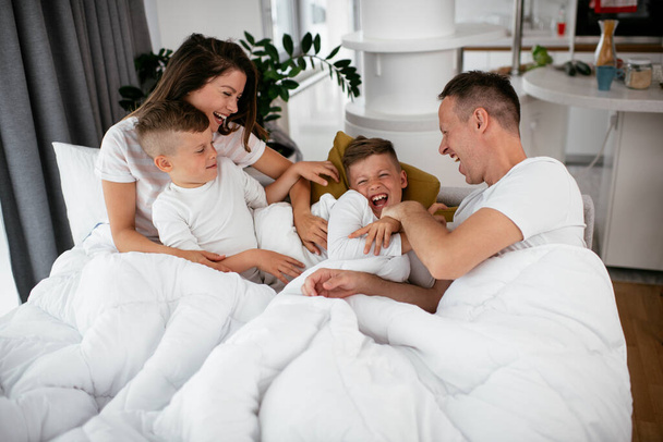 Młoda rodzina bawi się w łóżku. Szczęśliwi rodzice z synami relaksującymi się w łóżku. - Zdjęcie, obraz
