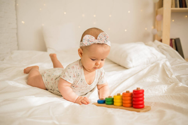 κοριτσάκι παίζει με ένα εκπαιδευτικό παιχνίδι στο κρεβάτι στο δωμάτιο.Πρόωρη ανάπτυξη του παιδιού - Φωτογραφία, εικόνα