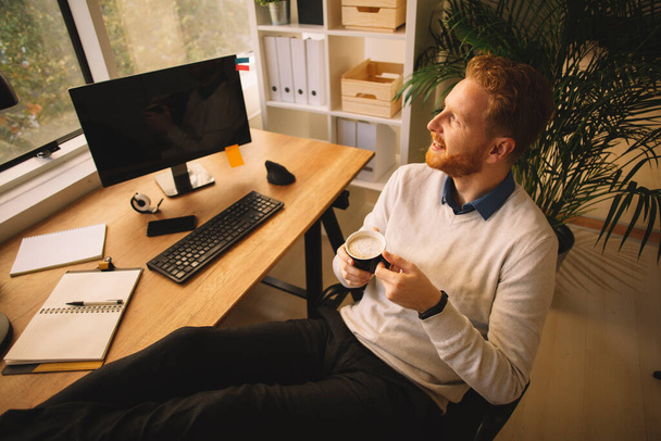 pohledný podnikatel s červenými vlasy pití kávy v kanceláři - Fotografie, Obrázek