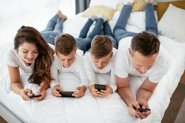 Familia usando teléfonos móviles. Padres e hijos usando teléfonos inteligentes en casa. - Foto, imagen