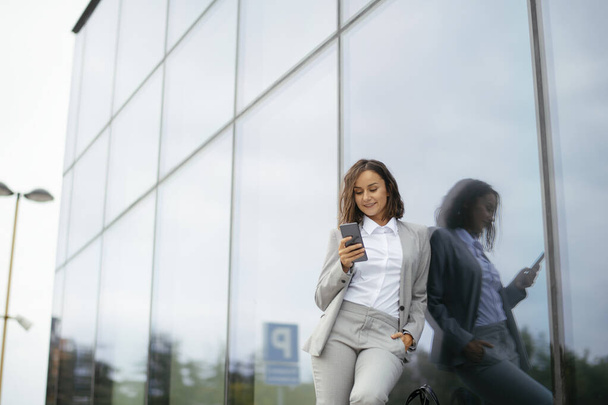 Udane młoda bizneswoman lub przedsiębiorca za pomocą telefonu podczas spaceru na świeżym powietrzu. Miasto biznesu kobieta pracy. - Zdjęcie, obraz