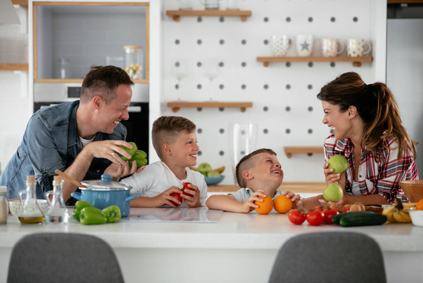 Mutter und Vater frühstücken mit ihren Söhnen. Junge Familie bereitet leckeres Essen in Küche zu und hat Spaß - Foto, Bild