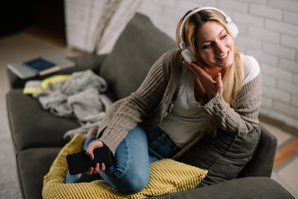 Close-up portrait of young beautiful woman listening to music. Woman listening music in headphones at her home. - Photo, Image