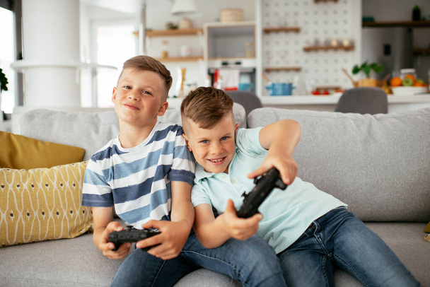 Young brothers having fun while playing video games in living room - Photo, Image