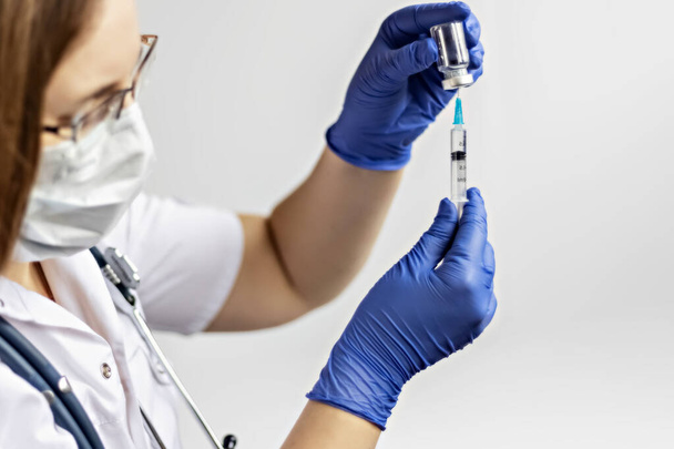 Eine Ärztin mit medizinischer Maske zieht den Coronavirus-Impfstoff in eine Spritze in der Klinik. Das Konzept der Impfung, Immunisierung, Prävention gegen Covid-19 - Foto, Bild