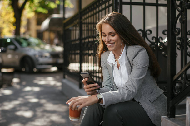 Portret młodej bizneswoman na ulicy ze słuchawkami i telefonem - Zdjęcie, obraz