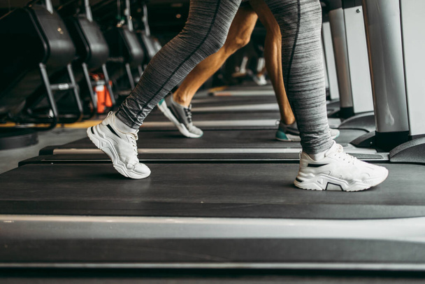 Young fit woman and man running on treadmill in modern fitness gym. Close up shot on moving legs. - Valokuva, kuva