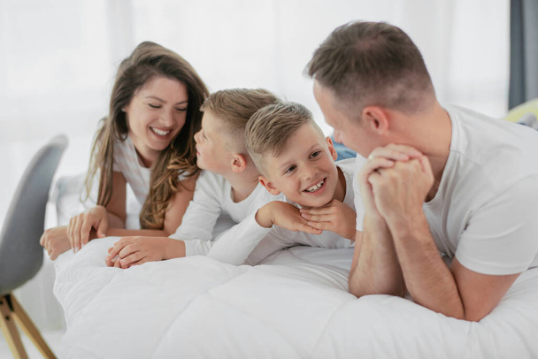 Junge Familie genießt im Bett. Glückliche Eltern mit Söhnen, die sich im Bett entspannen - Foto, Bild