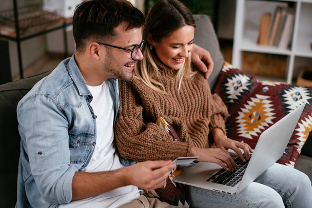 Young couple using credit card and laptop at home. Boyfriend and girlfriend buying online. - Photo, Image