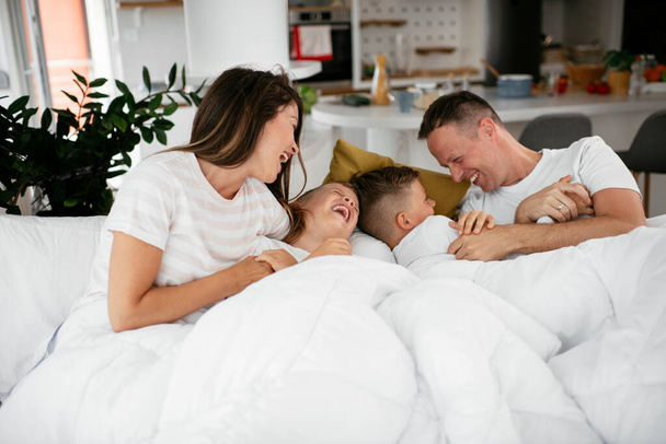 Jonge familie die geniet in bed. Gelukkig ouders met zonen ontspannen in bed. - Foto, afbeelding