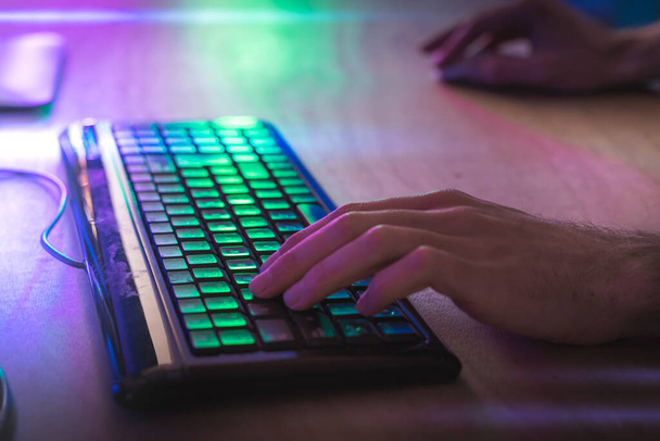 Close-up hands in keyboard of a professional gamer playing video game on his personal computer. Room lit by Neon Lights in Retro Arcade Style.Cyber Championship. Footage fade out into bokeh. - Foto, Imagen