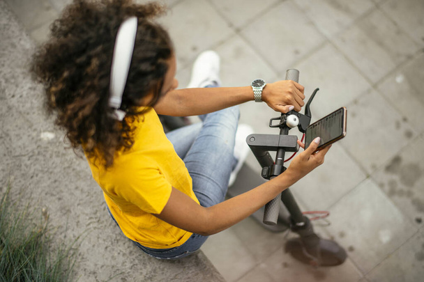 Fille en utilisant le téléphone et écouter de la musique tout en restant sur scooter électronique - Photo, image