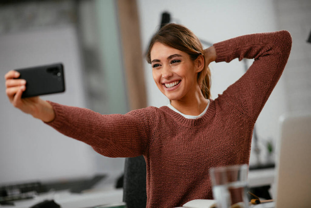 Portrét mladé hezké podnikatelky, která fotí selfie v kanceláři. Krásná žena brát selfie na pracovišti. - Fotografie, Obrázek