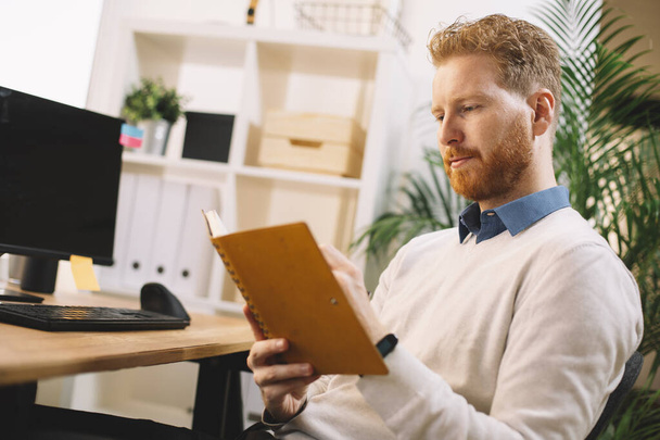 νεαρός όμορφος επιχειρηματίας διαβάζει σημειώσεις στο γραφείο - Φωτογραφία, εικόνα