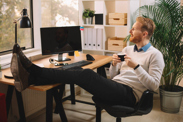 knappe zakenman met rood haar die koffie drinkt op kantoor - Foto, afbeelding