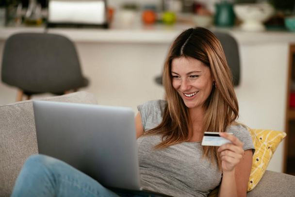Young woman using her credit card and laptop at home. Beautiful woman buying online. - Fotoğraf, Görsel
