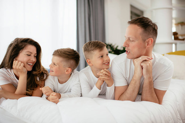 Familia joven disfrutando en la cama. Padres felices con hijos relajándose en la cama - Foto, imagen