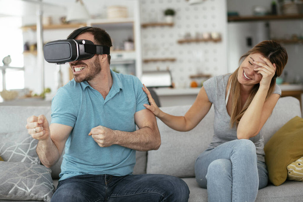 Щаслива пара розважається з окулярами віртуальної реальності у вітальні. Молода пара грає і насолоджується відеоіграми з гарнітурою VR вдома
. - Фото, зображення