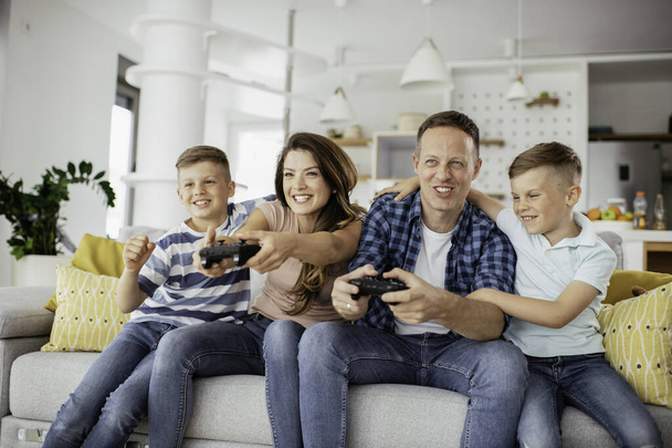 Padre y madre se divierten mientras juegan videojuegos con niños en casa. - Foto, Imagen