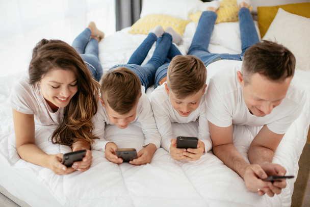 Familia usando teléfonos móviles. Padres e hijos usando teléfonos inteligentes en casa. - Foto, imagen
