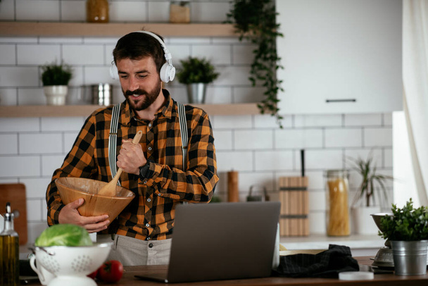 Retrato de un hombre guapo en la cocina. Hombre joven cocinar mientras usa el ordenador portátil. - Foto, Imagen