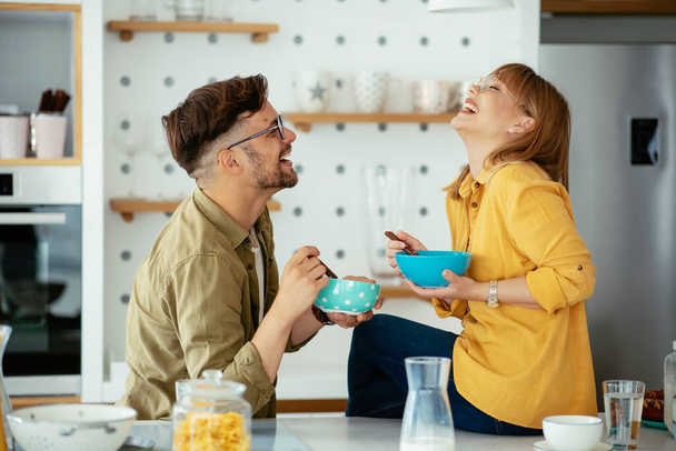 Genç çift evde kahvaltı hazırlıyor. Sevgi dolu çift mutfakta mısır gevreği yiyor.. - Fotoğraf, Görsel