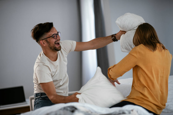 Mladý pár bojuje s polštáři na posteli. Šťastný pár se baví doma - Fotografie, Obrázek