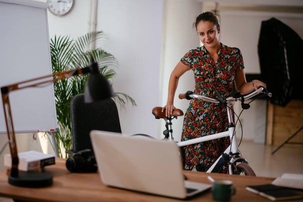 Fiatal nő áll az irodában kerékpárral  - Fotó, kép