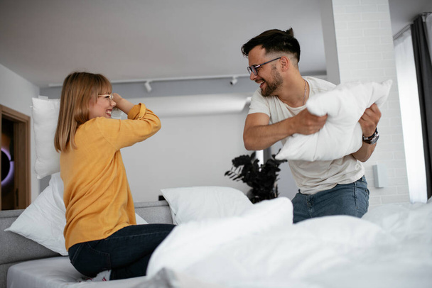 Młoda para walcząca poduszki na łóżku. Szczęśliwa para bawiąca się w domu - Zdjęcie, obraz
