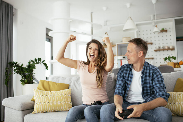 Vriendje en vriendinnetje spelen videospel met joysticks in de woonkamer. Liefdevol paar spelen videospelletjes thuis. - Foto, afbeelding