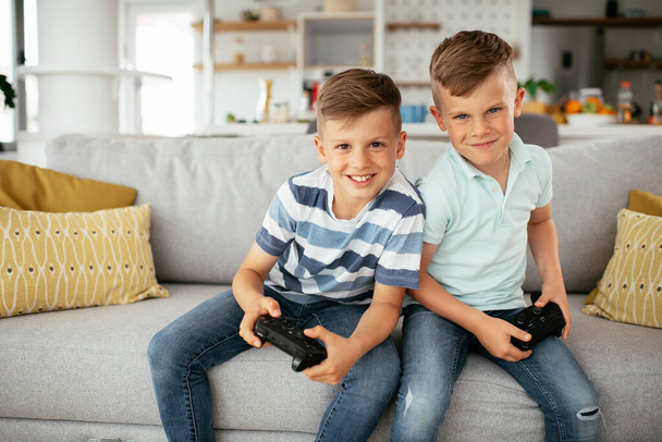 Happy brothers playing video games. Young brothers having fun while playing video games in living room - Фото, зображення