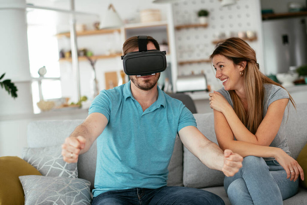 Happy couple having fun with virtual reality glasses in living room. Young couple playing and enjoying video games with VR headset at home. - Photo, Image
