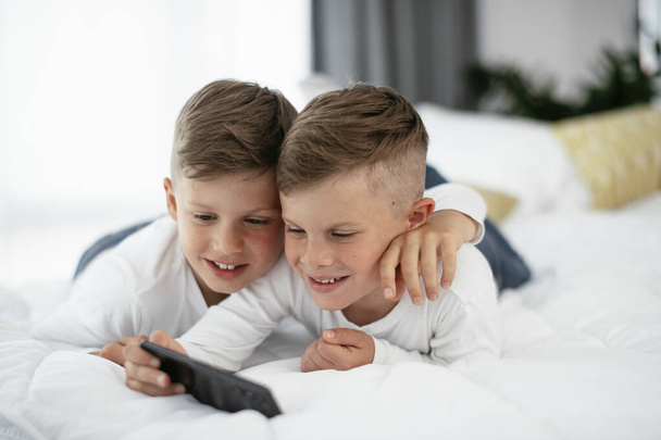 Two little brothers are playing games on the phone. Beautiful boys enjoying at home. - Photo, Image