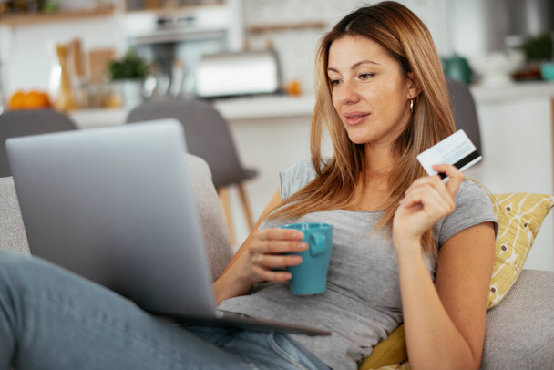 Молода жінка використовує свою кредитну картку і ноутбук вдома. Красива жінка купує онлайн
. - Фото, зображення