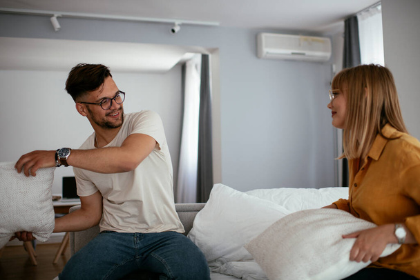 Young couple fighting pillows on the bed. Happy couple having fun at home - 写真・画像