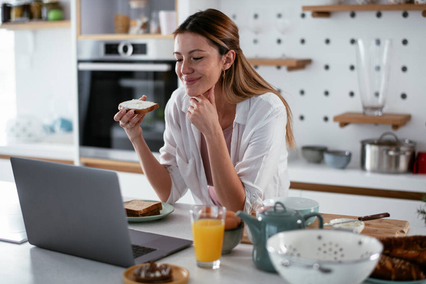 Mujer joven disfrutando de su desayuno mientras trabaja en el portátil - Foto, imagen