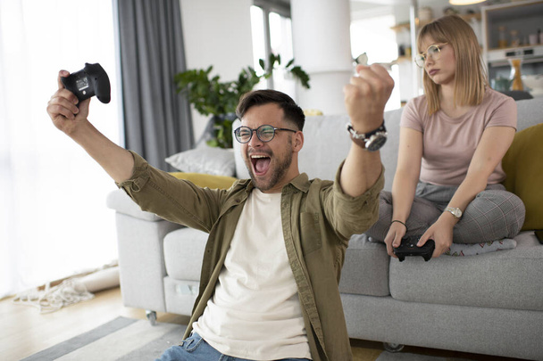 Man en vrouw spelen videospel met joysticks in de woonkamer. Liefdevol paar spelen videospelletjes thuis. - Foto, afbeelding