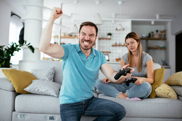 Man en vrouw spelen videospel met joysticks in de woonkamer. Liefdevol paar spelen videospelletjes thuis. - Foto, afbeelding