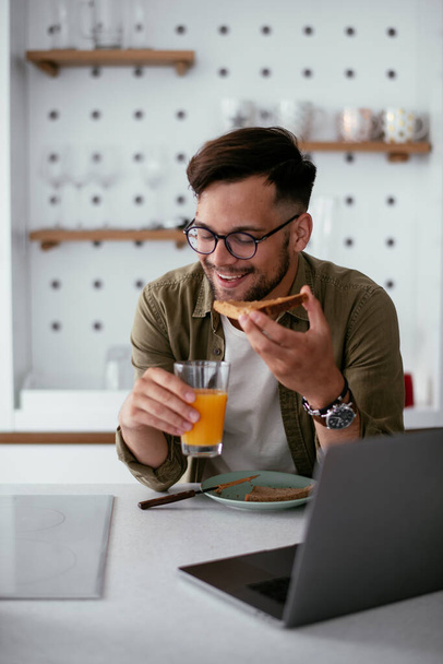 Молодий чоловік їсть сніданок і читає новини онлайн. Красивий чоловік насолоджується вдома
. - Фото, зображення