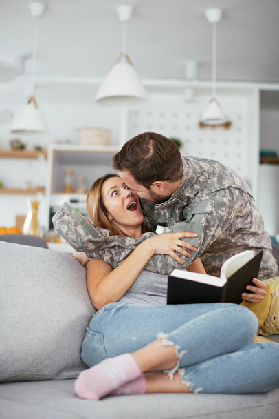 Ευτυχισμένος στρατιώτης κάνει έκπληξη στη γυναίκα του στο σπίτι. Νεαρή στρατιώτης αγκαλιάζει τη σύζυγο. - Φωτογραφία, εικόνα