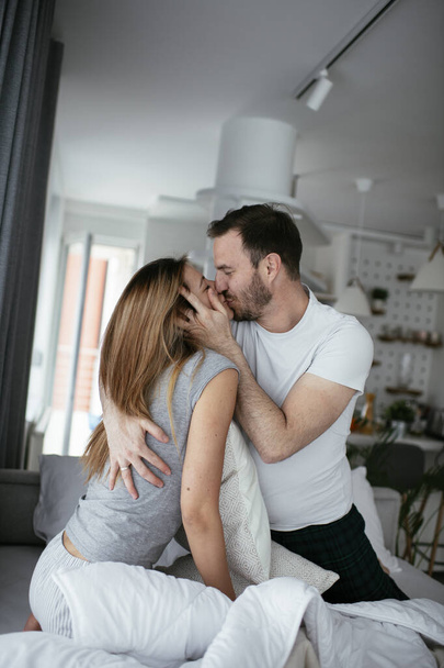 Young couple fighting pillows on the bed. Happy couple having fun at home - Фото, изображение