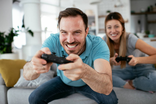 Mari et femme jouant à un jeu vidéo avec des joysticks dans le salon. Couple aimant jouent à des jeux vidéo à la maison. - Photo, image