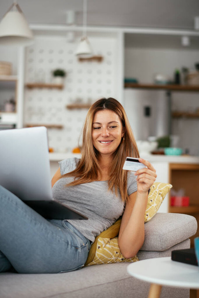 Молодая женщина использует свою кредитку и ноутбук дома. Красивая женщина покупает онлайн. - Фото, изображение