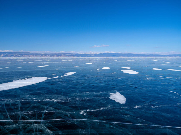 Aerial panoramic view of the Baikal lake at winter season. Spiderweb cracks on frozen ice surface and far mountain on horizon under clear blue sky. Beautiful landscape, perspective view from high. - Zdjęcie, obraz