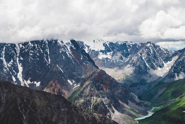 Atmosferyczny alpejski krajobraz z ogromnym wiszącym lodowcem na olbrzymich skałach i doliną z jeziorami górskimi. Duży język lodowca. Niskie chmury nad śnieżnymi górami. Majestatyczne krajobrazy na dużej wysokości. - Zdjęcie, obraz
