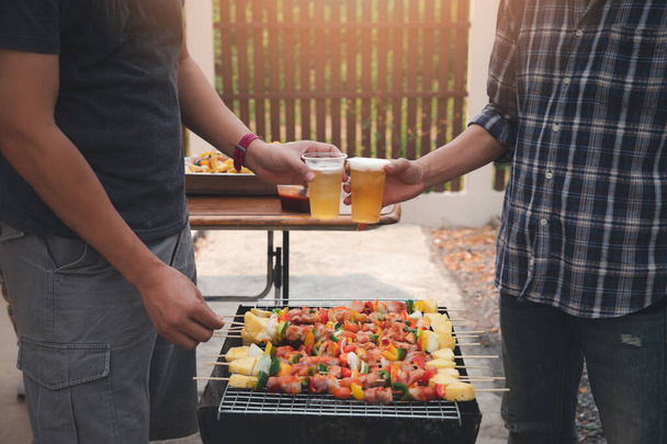 Les jeunes hommes applaudissent pour un verre lors d'une soirée barbecue entre amis. Nourriture, boisson, personnes et concept de temps en famille. - Photo, image